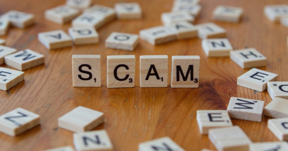 Scam word spelled with wooden letter blocks on table - fraud warning and import scam concept