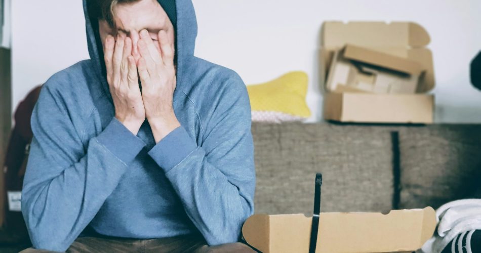 A man covering his face with both hands in frustration after an online shopping return issue